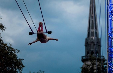 An acrobat swings through the air as a church spire can be seen in the background