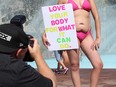 a woman poses with belly, stretch marks exposed, holding a sign: love your body for what it can do