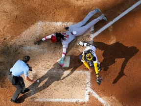Top-down view shows Cincinnati Reds' Elly de la Cruz sliding head-first into home as the baseball goes by the catcher