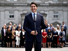 Justin Trudeau stands at a microphone outside while his cabinet ministers line up far behind him
