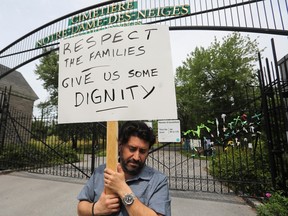 Jimmy Koliakodakis holds a sign saying "Respect the families. Give us some dignity" outside Notre-Dame-des-Neiges Cemetery