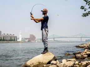 A man standing on a rock casts a fishing line with the city skyline in the background