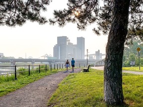 a couple walks next to the peel basin with a smoggy montreal skyline in the background