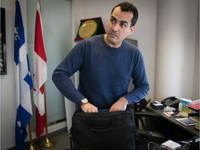 Monsef Derraji in a blue long-sleeve shirt puts documents in his briefcase while standing next to his desk