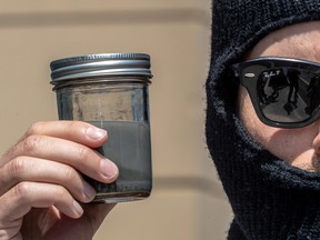 A masked man holds a jar of grey water