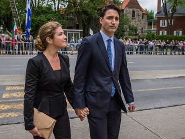 Sophie Grégoire, dressed in black, looks at Justin Trudeau as they walk holding hands on a sidewalk. A crowd behind barricades can be seen in the background.