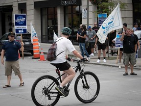 a cyclist bikes past striking blue collar workers
