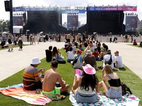 People sit on a grassy area facing an outdoor stage in the distance