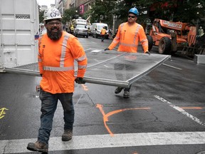 Two construction workers carry a segment of temporary fencing on a closed street