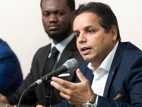 Abdelhaq Sari gestures while at a microphone next to Philippe Thermidor