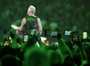 James Hetfield is seen from behind through a group of fans holding up their phones at a Metallica concert