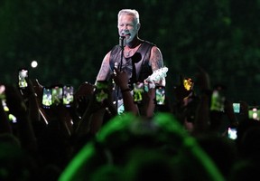 James Hetfield is seen through a group of fans holding up their phones at a Metallica concert