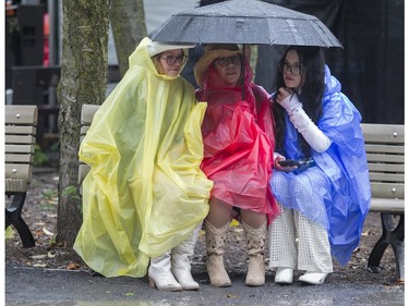 Rosie Di Lorio (centre) and her daughters Emma Sotos (left) and Alexa Dal Santo huddle under an umbrella at the Lasso country-music festival at Parc Jean-Drapeau in Montreal on Saturday, Aug. 19, 2023.