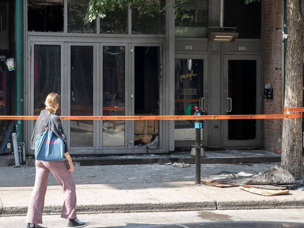 A person walks past police tape in front of a building at 3612 St Laurent that was fire bombed early on Aug. 21, 2023.