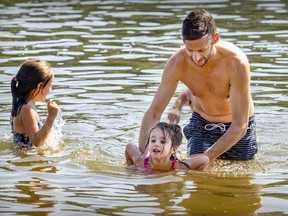 a father helps his young daughter float in the water while another daughter watches
