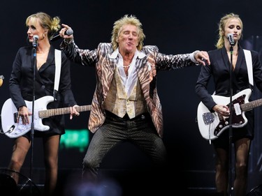 Flanked by two female guitarists, Rod Stewart strikes a pose on stage