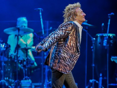 Rod Stewart struts across a stage lit in blue during a concert