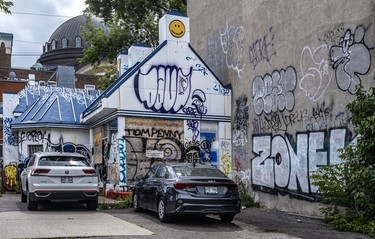 A former gas station with a yellow happy face sign still there, but otherwise covered in graffiti, with two cars parked outside.