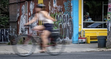 A man sits in the window seat at Lloydies restaurant, a graffiti-coated, yellow-facaded building, on St-Viateur St. as the blurred image of a cyclist whizzes by.