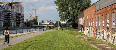 A view of condos overlooking the Lachine Canal as a jogger passes a brick wall filled with graffiti.