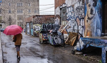 A woman with red umbrella walks through the graffiti-covered alley behind the Sherwin-Williams Paint store on Atwater Ave.