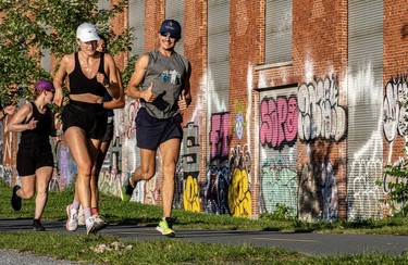 Four runners jog past graffiti along a paved path on the Lachine Canal between Atwater Market and the Peel Basin.
