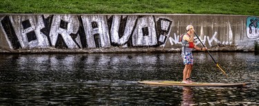 A paddle boarder in life jacket drifts by graffiti along the Lachine Canal east of Atwater Market.