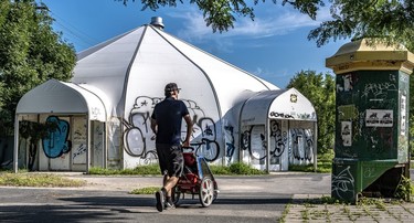Graffiti coats a white domed tent structure near Parc Ovila-Pelletier as a man in shorts and cap walks by with a stroller.