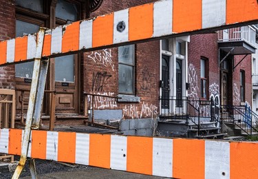 An orange traffic barrier blocks entrance to graffiti-covered row houses on St-Urbain St.