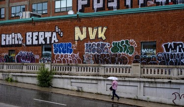 An umbrella-carrying man walks up a steep incline on Park Ave., past colourful graffiti on the Holland Varnish Company building.