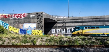 Graffiti on a railway tunnel near the Turcot Interchange as a green and yellow VIA train speeds by.