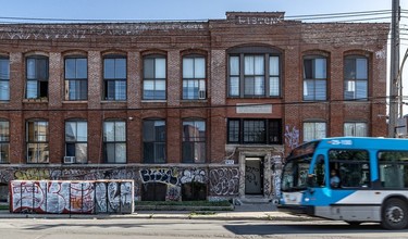 A blue Montreal city bus passes by the graffiti-covered three-storey former Fattal brick building.