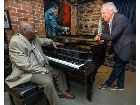 Jim West leans over a piano while speaking with Oliver Jones sitting behind the keys in a corner of a bar