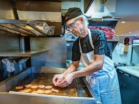 A man is placing pieces of pepperoni on a grill at a diner.