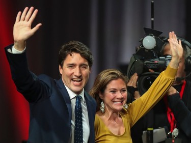 Justin Trudeau and Sophie Grégoire Trudeau smile and wave with a news video camera behind them