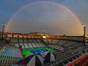 A rainbow is seen above a mostly empty IGA Stadium near sunset with two umbrellas in the foreground