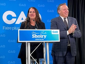 Marie-Anik Shoiry smiles behind a podium with her name on it and the CAQ logo behind her on stage next to François Legault