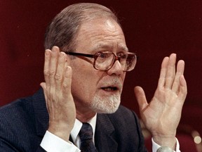 Photo of a man in glasses raising both hands as he speaks