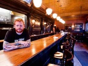 Derek Dammann leans on the counter at an empty wooden bar