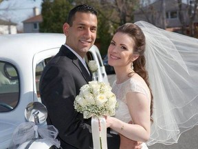 A couple in wedding attire lean against a classic car outside