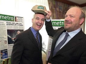 Pelle Tornberg puts a Métro-branded hat on a laughing André Préfontaine with mockups of the Métro newspaper front page behind them
