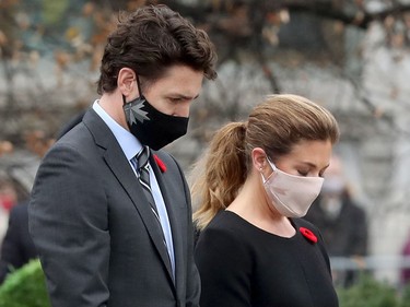 Justin Trudeau and Sophie Grégoire Trudeau, wearing masks, look down with poppies on their chests
