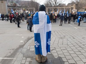 A man has a Quebec flag draped around his back facing a protest