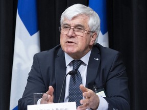 Photo of a man speaking at a press conference in front of a Quebec flag