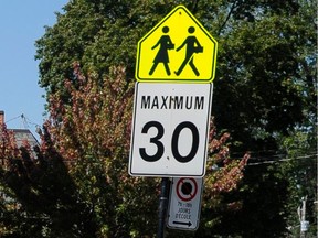 A school zone traffic sign and a 30 km/h speed limit sign on a pole outside