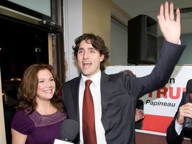 Justin Trudeau waves next to a smiling Sophie Grégoire Trudeau at the entrance to an office with a campaign sign in the background