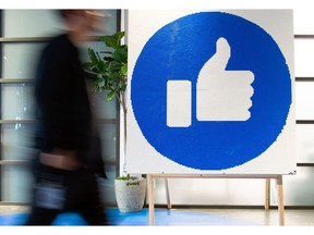 Blurred image of a man walking by a poster of Facebook's blue like symbol.