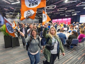 Two women carrying orange CSN flags leave a conference hall. Other labour activists are following them.
