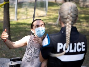 A police officer is seen from behind, speaking to a man wearing a mask and sitting in a wheelchair.