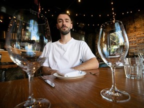 Restaurant owner Jules Dubé of Provisions restaurant gazes between wine glasses at the camera.